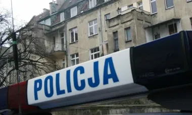 Policyjny kogut na tle kamienicy.