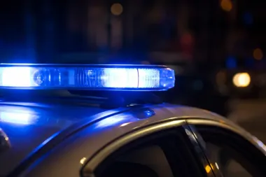 Nocne ujęcie policyjnego radyjka z włączonym niebieskim światłem na dachu radiowozu.